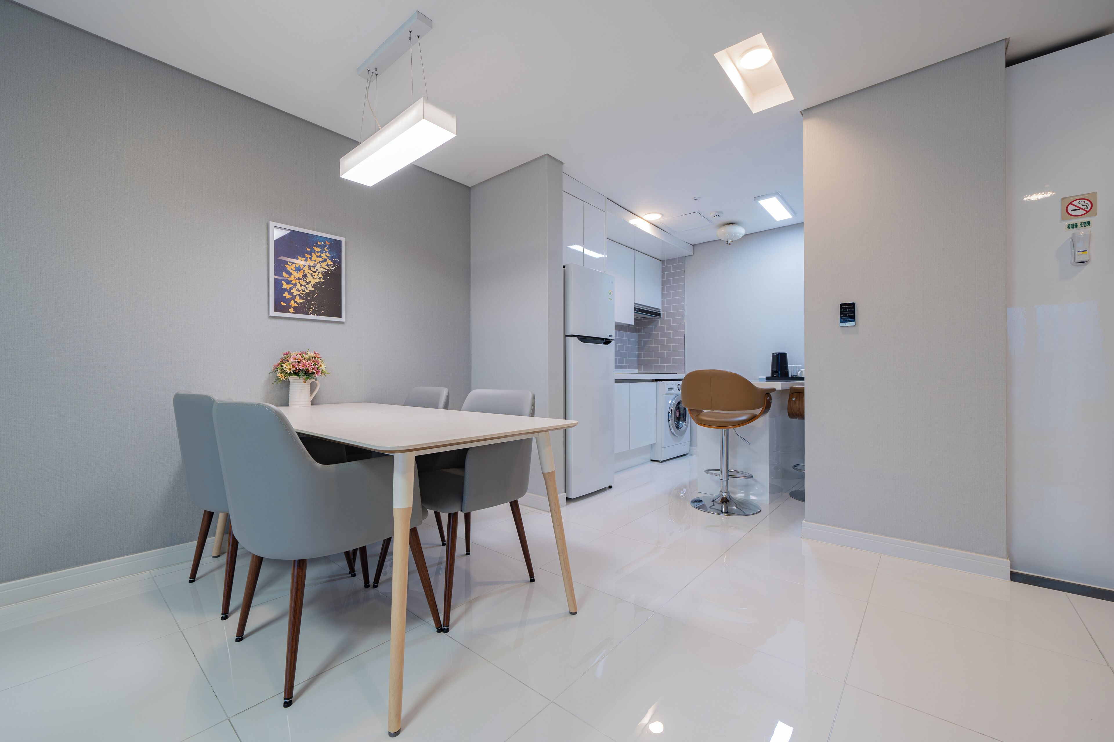 A modern kitchen with white appliances, a dining area with a white table and chairs, and a small seating area with a stool.
