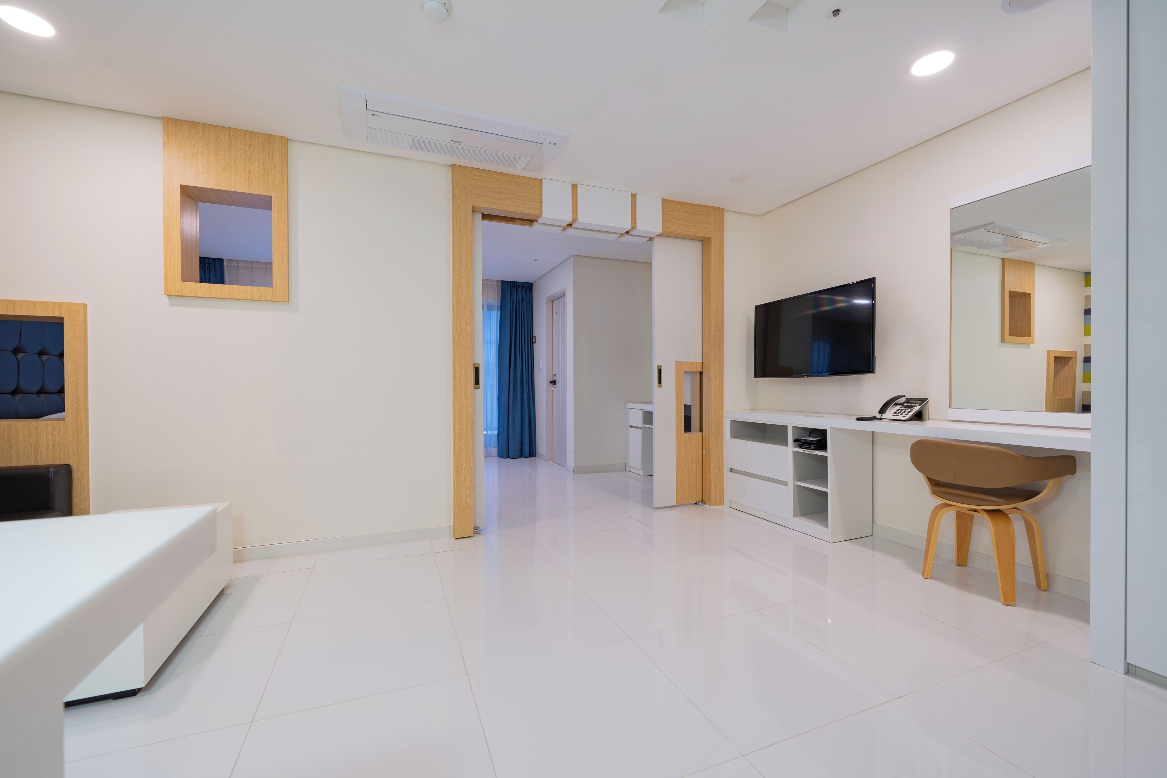 A modern hotel room with a white reception desk, a television, a desk chair, and a large mirror.