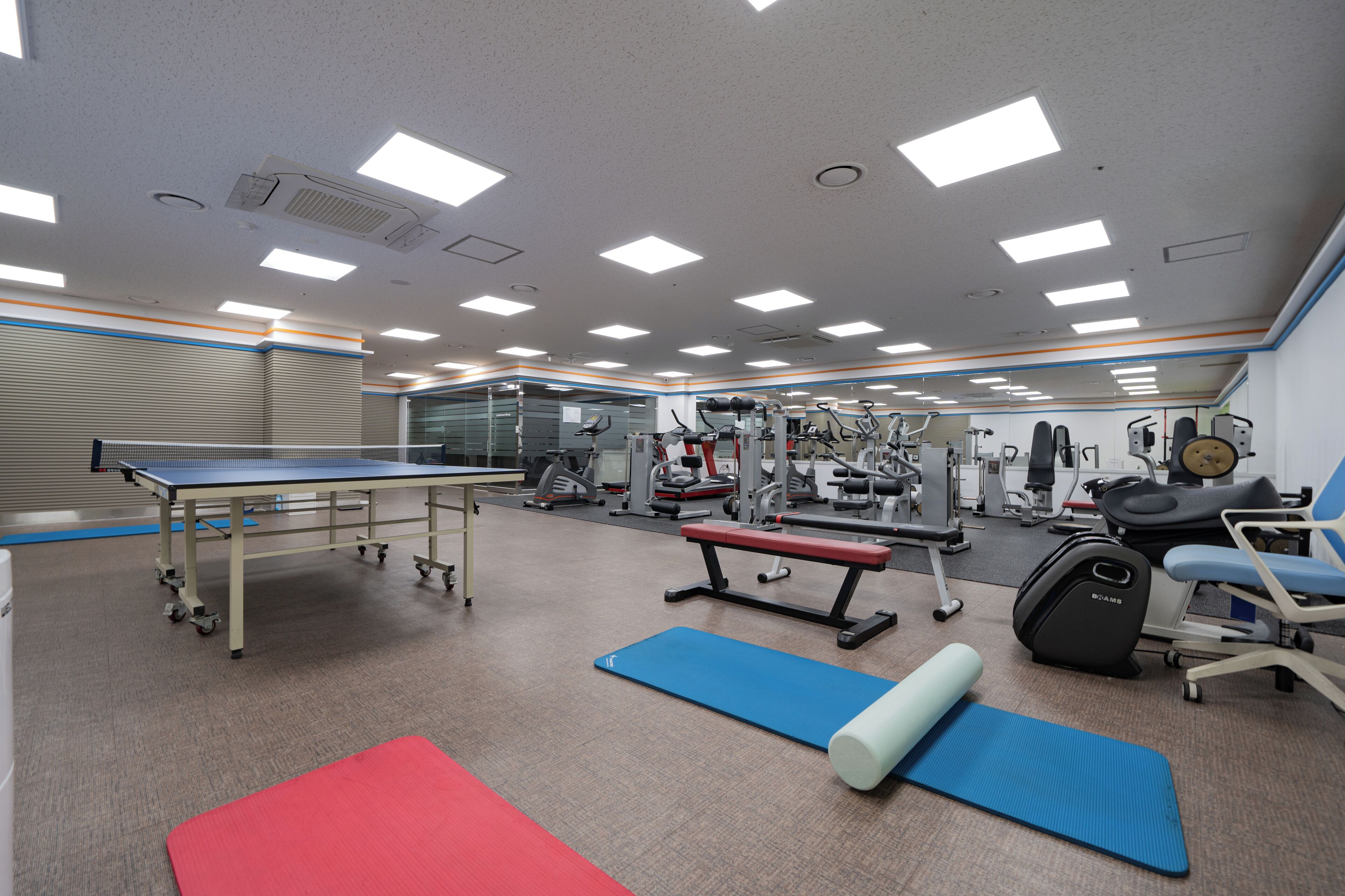 A gym with exercise equipment, a ping pong table, and a mirror.