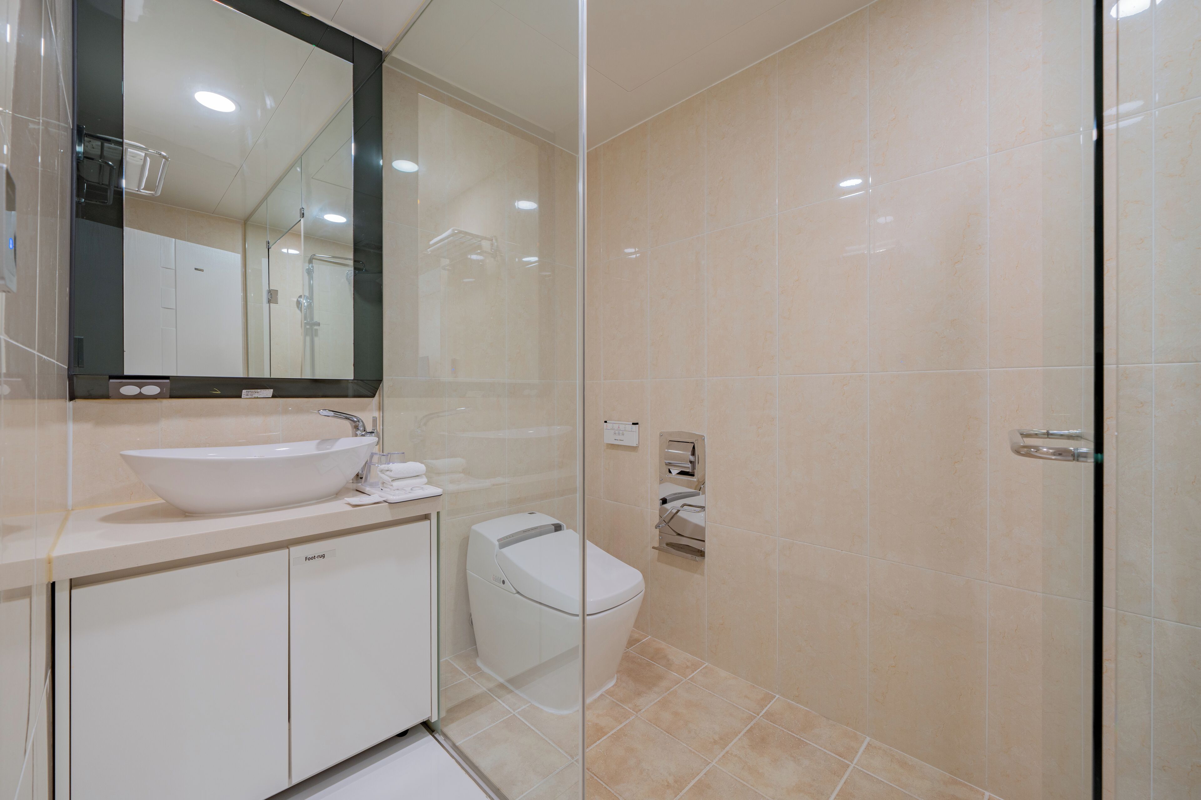 A modern bathroom with a large mirror, a sink, a toilet, and a glass shower enclosure.