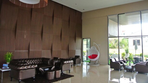 A modern lobby with leather sofas, a red egg chair, and a large glass window offering a view of the outdoors. - Himawari at Condo (Khon Kaen)
