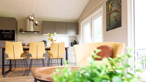 A modern kitchen with a dining area, featuring a central island, yellow chairs, and a sofa with a brown pillow. - TopParken Parc de IJsselhoeve (Nieuwerkerk aan den IJssel)