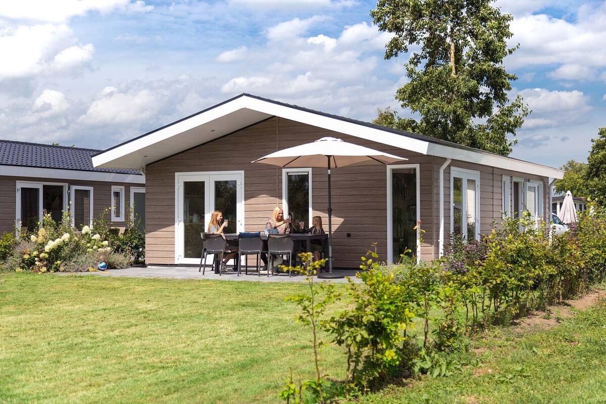 Ein modernes Haus mit einer überdachten Terrasse, an der Tische mit Sitzgelegenheiten stehen.
