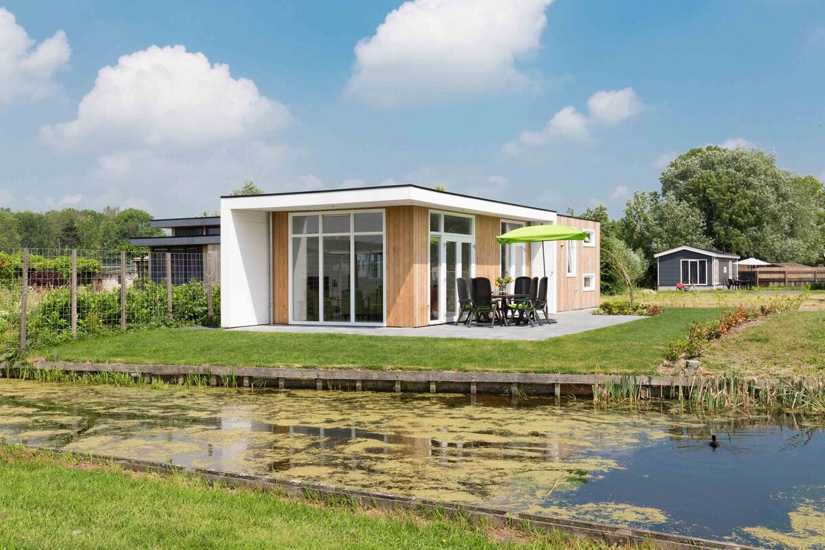 Ein modernes Haus mit Terrasse, Teich und einem eingezäunten Garten.