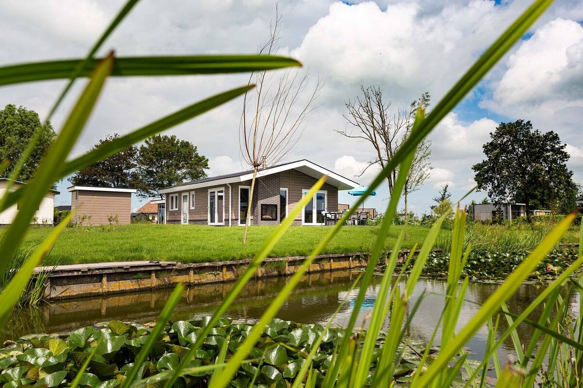 Ein modernes Haus mit Rasengrundstück und Teich im Vordergrund.