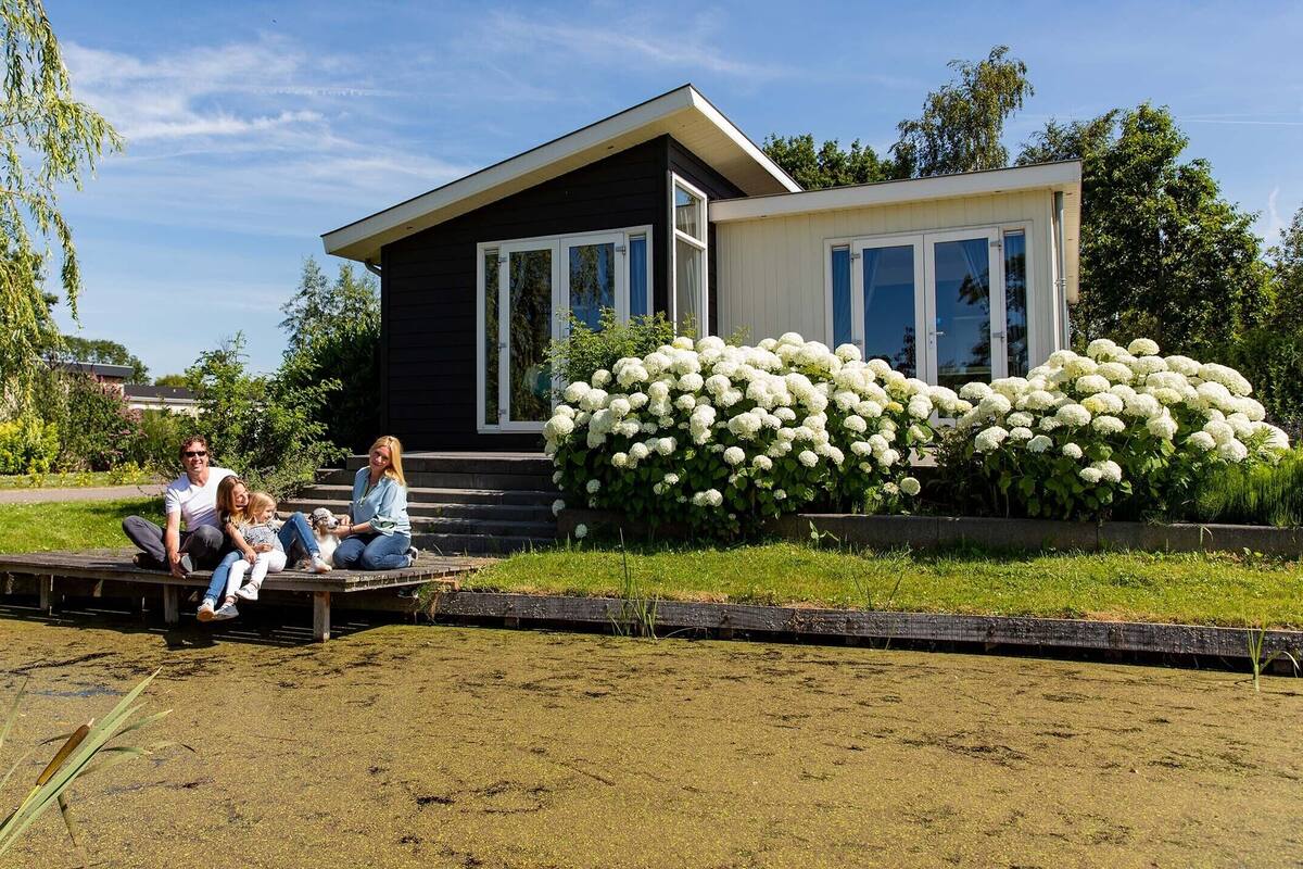 Ein modernes Haus mit schwarzem Außenbereich und weißem Zierstreifen, einer Veranda und einem Garten mit weißen Hortensienbüschen.