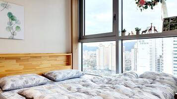 A bedroom with a large bed, a wooden headboard, a city view through a large window, and a wall-mounted plant.
