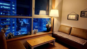 A modern living room with a sofa, a wooden table, and a window with a city view. - DG HOUSE (Daegu)