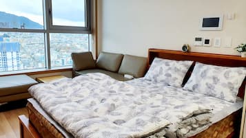 A bedroom with a bed, a bench, and a view of a cityscape through large windows.