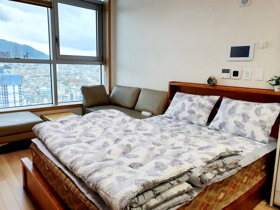A bedroom with a bed, a bench, and a view of a cityscape through large windows.