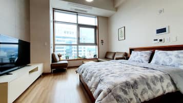 Moderni hotellihuone, jossa on suuri sänky, televisio, ikkuna, josta avautuu näkymä kaupunkiin, sekä oleskelualue, josta on myös näkymä.