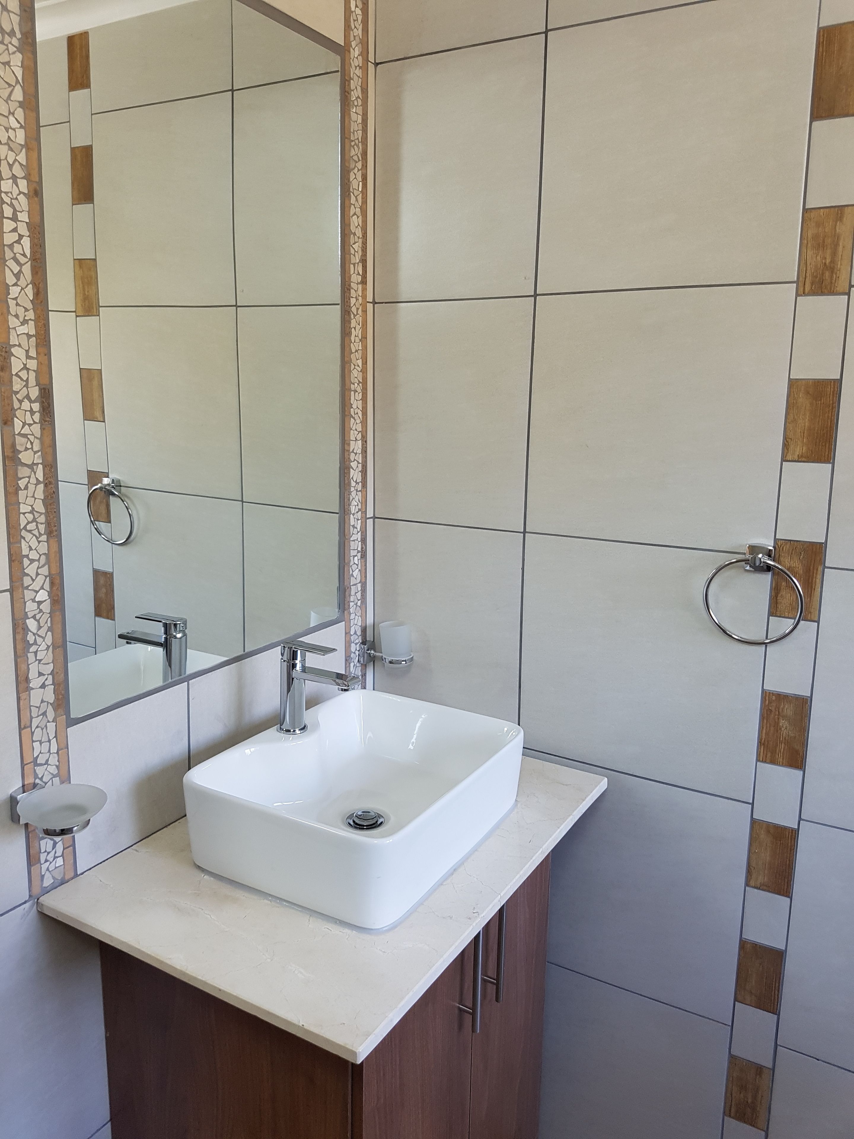 A bathroom with a white sink, a mirror, and a tiled wall with a geometric pattern.