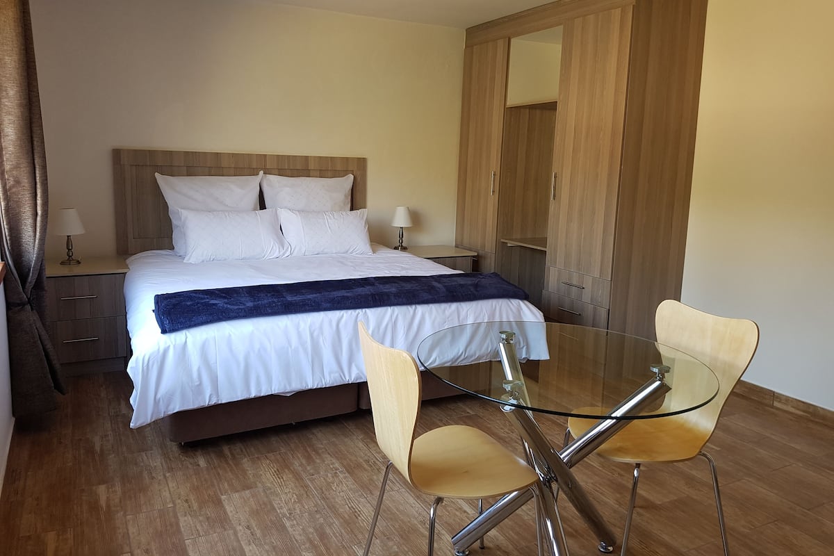 A bedroom with a bed, bedside tables, a wardrobe, and a glass table with chairs.