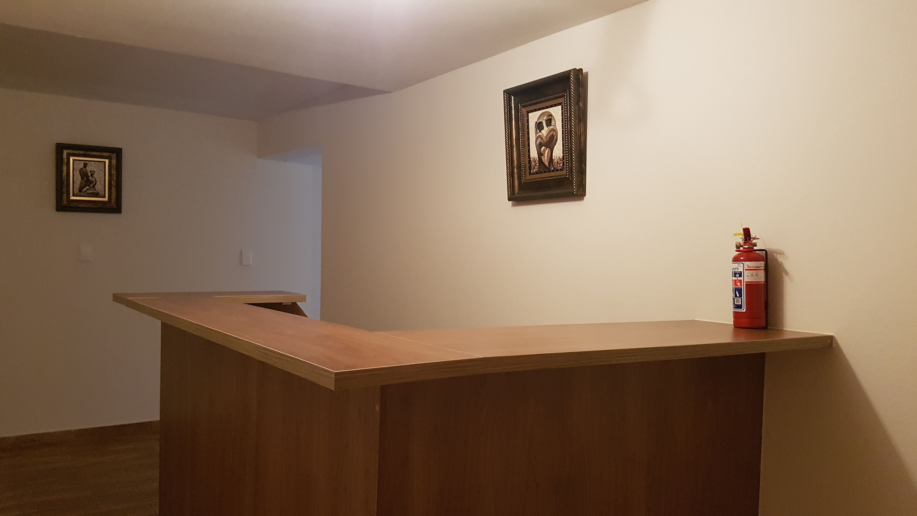 A room with a wooden reception desk, a framed picture on the wall, and a fire extinguisher.