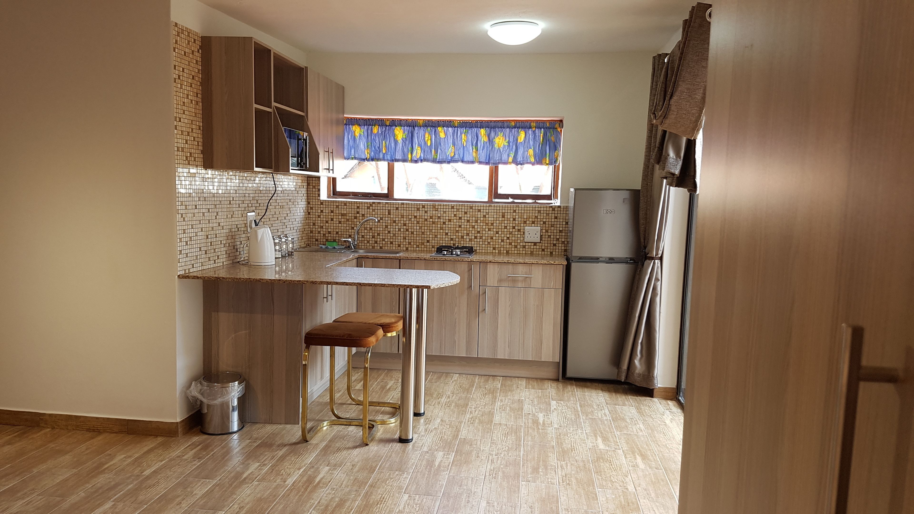 A compact kitchen with a built-in sink, a refrigerator, and a window with a blue curtain.