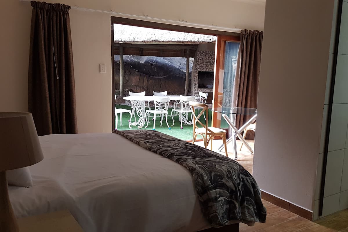 A bedroom with a large bed, a view of an outdoor patio with white chairs and a table, and a sliding glass door.