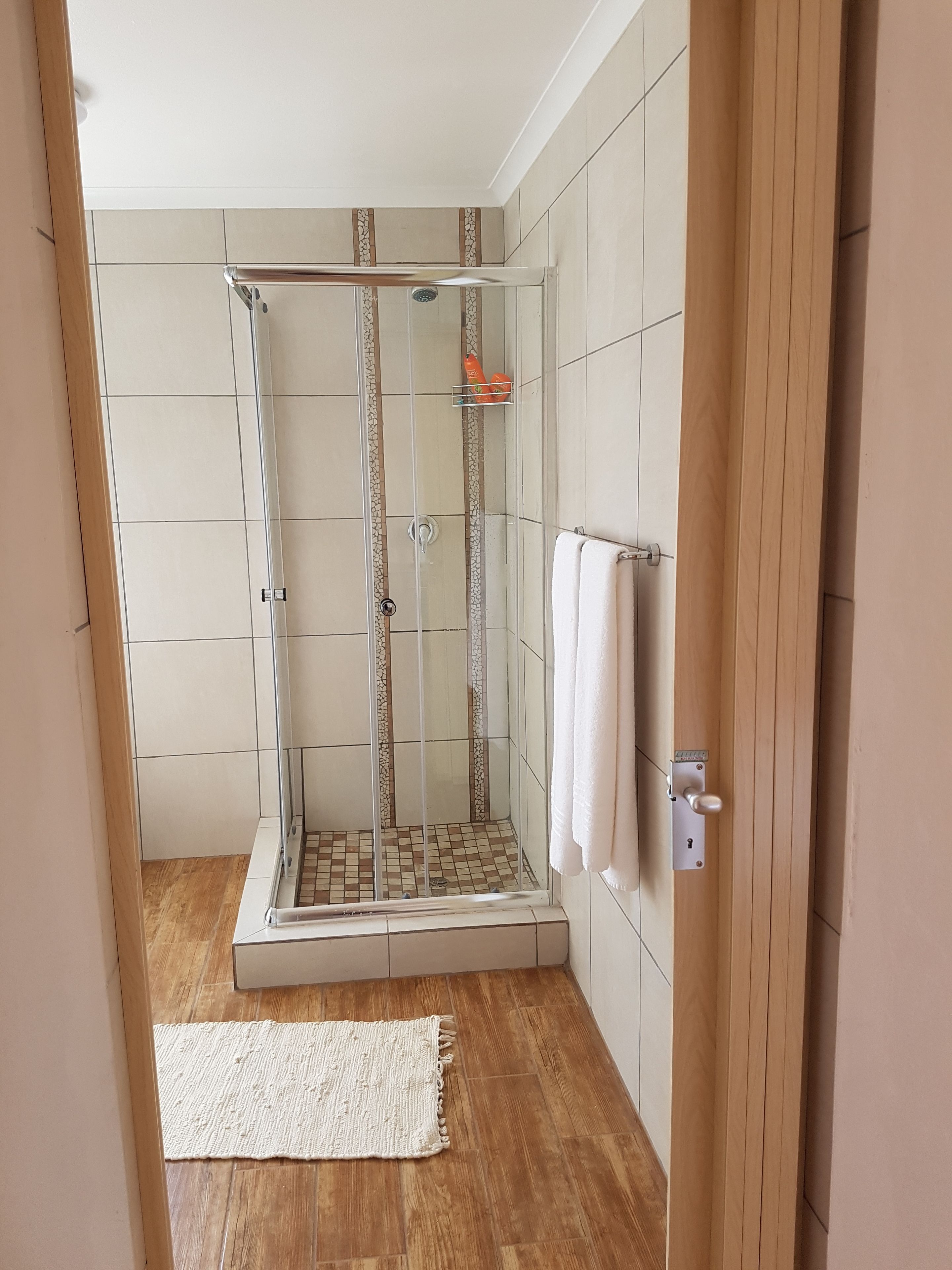 A shower with a glass door, a white towel hanging on the wall, and a small shelf with toiletries.