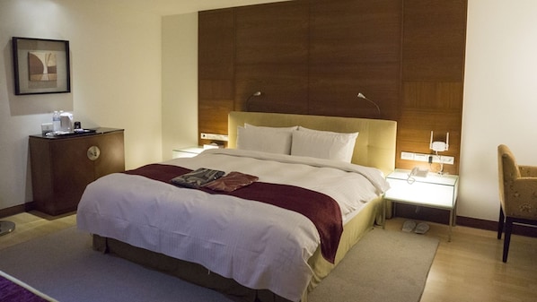 A hotel room with a large bed, bedside tables with lamps, a wooden headboard, a framed picture on the wall, and a small desk with a phone.
