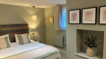 A hotel room with a bed, bedside lamp, framed artwork, and a vase with flowers.