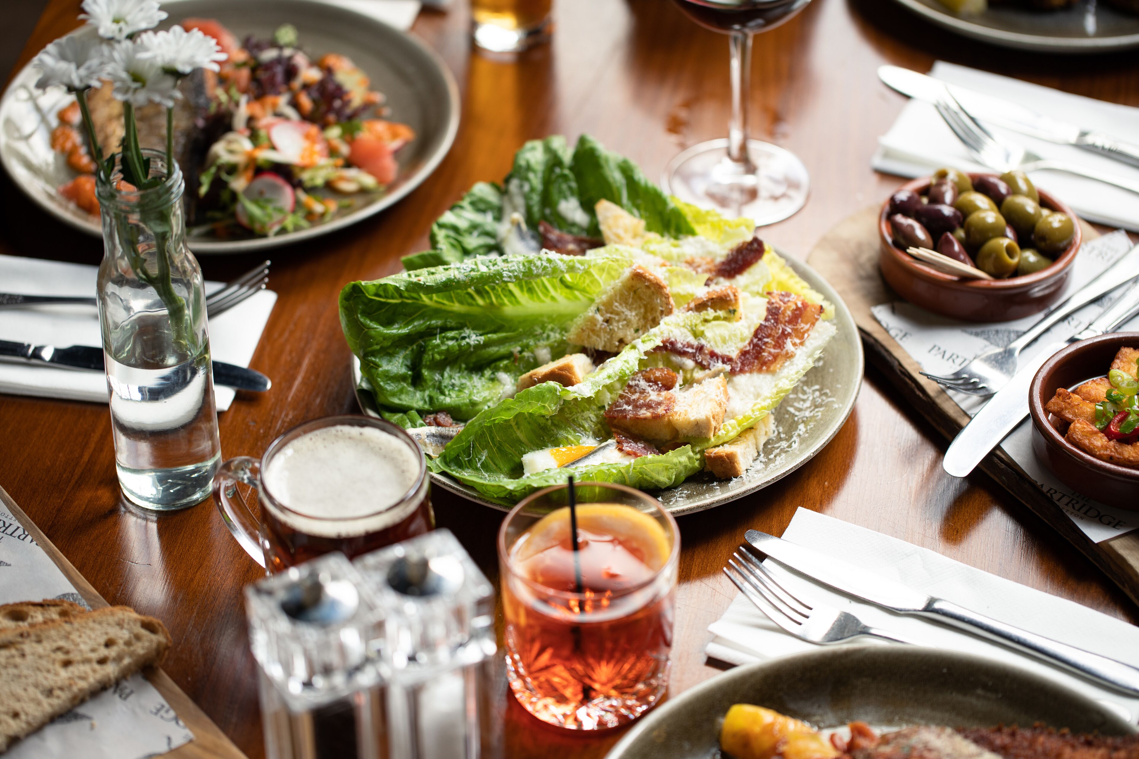 Een eettafel met verschillende gerechten, waaronder een salade, brood en een schaal olijven.