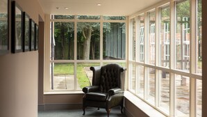 Een kamer met een groot raam, een leren fauteuil en een lijst met foto’s aan de muur.