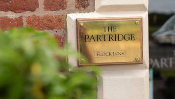 Uma placa de latão numa parede branca com o texto "THE PARTRIDGE FLOCK INNS".