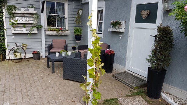 A covered patio with outdoor furniture, potted plants, and a bicycle. - Zimmervermietung Wesermarsch (Berne)