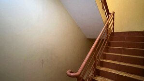 Una escalera con peldaños de madera y barandilla rosa, que conduce a un rellano con suelo de diseño geométrico.