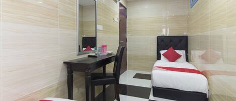 Una habitación de hotel con piso a cuadros, un escritorio con una silla, una cama con un almohón rojo y un espejo grande en la pared.