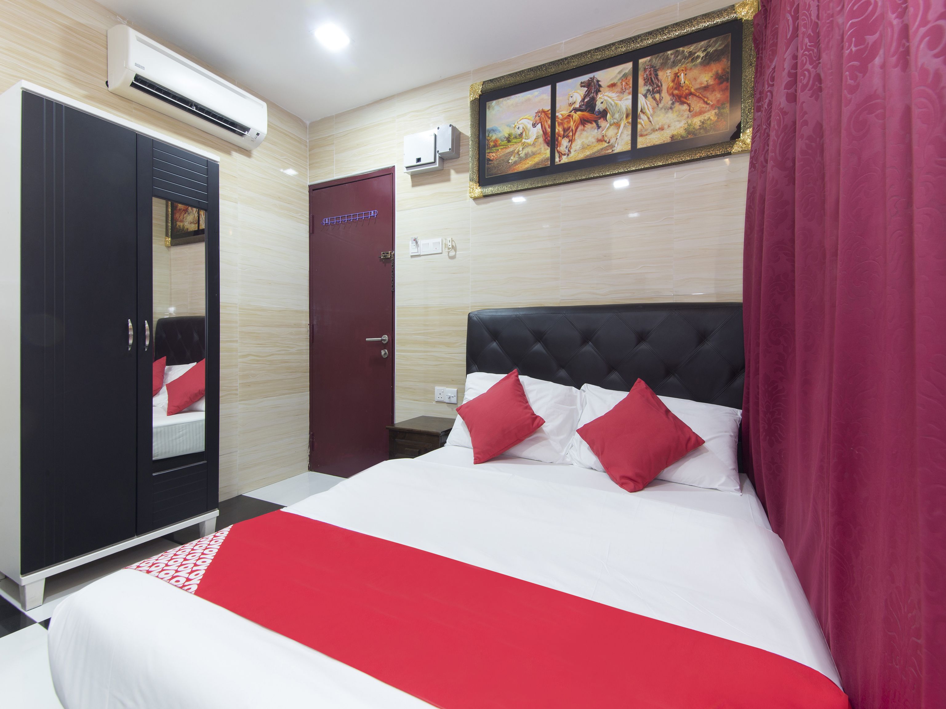 A hotel room with a bed, a wardrobe, a door, and an air conditioning unit.