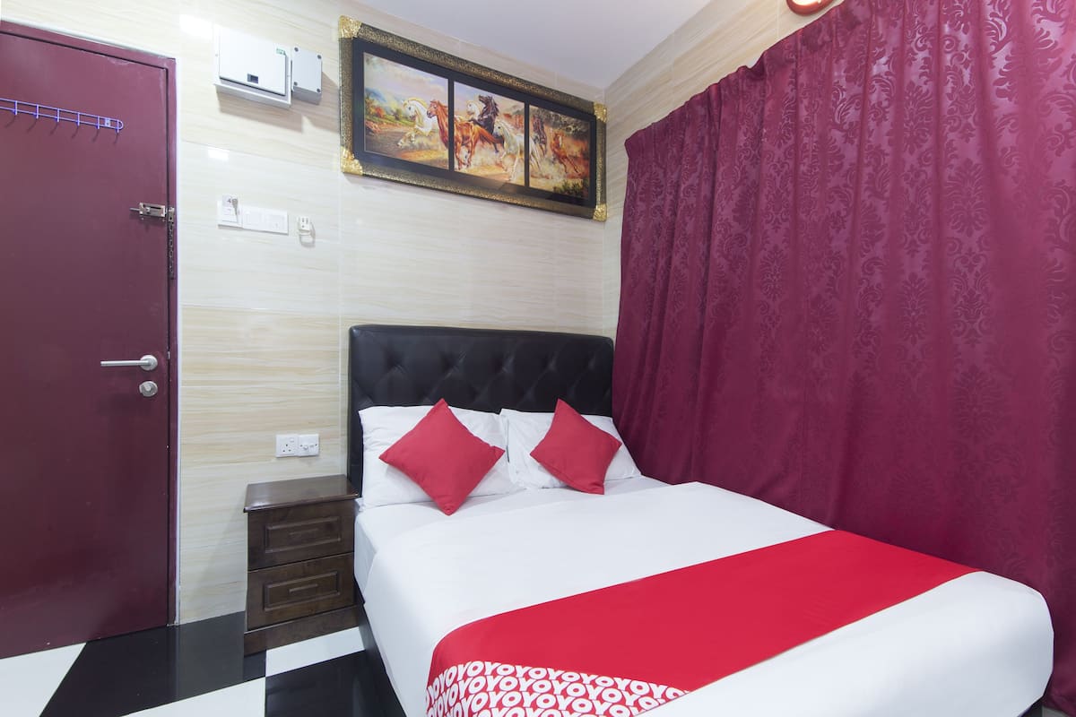 Une chambre d’hôtel avec un lit, une porte rouge, un tableau au mur et un rideau à motifs.
