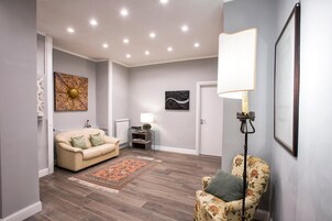 Een moderne woonkamer met een beige bank, een fauteuil met bloemenprint, een tapijt met patroon en een vloerlamp.