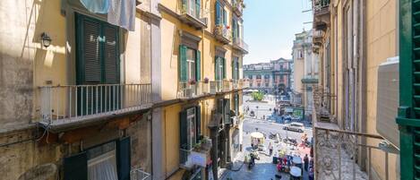 A narrow street with buildings on either side, balconies with laundry, and parked scooters.