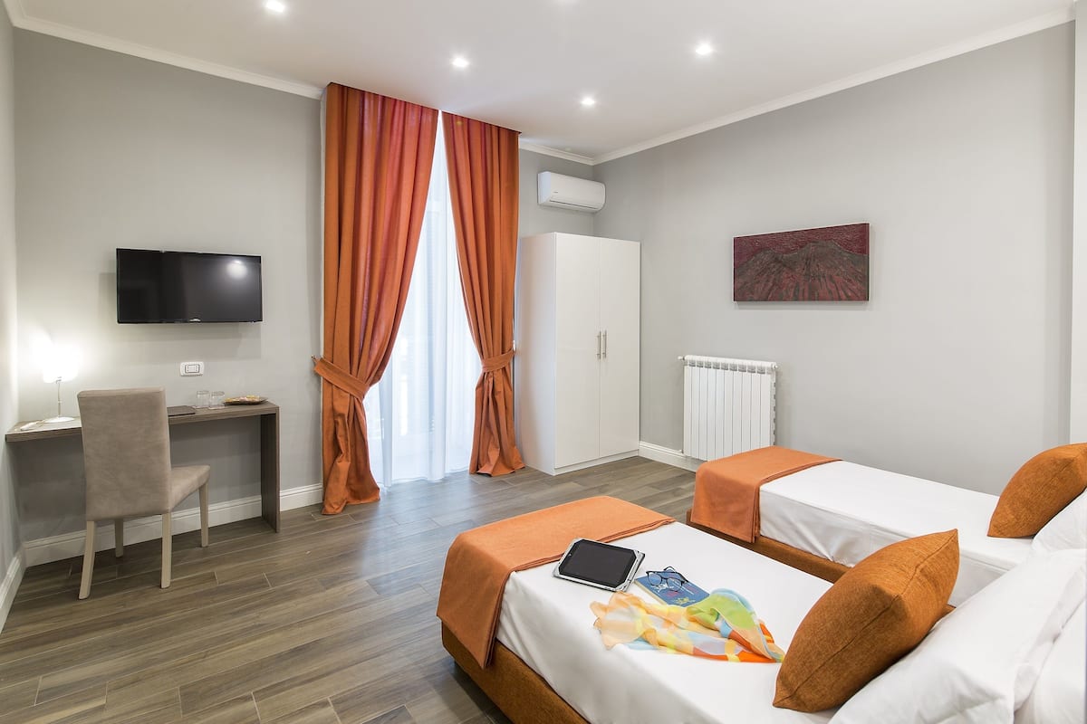 A hotel room with two beds, a desk, a chair, a TV, and a window with curtains.