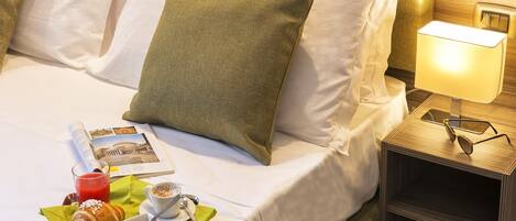 A neatly made bed with white linens, a green pillow, and a bedside table with a lamp and glasses.