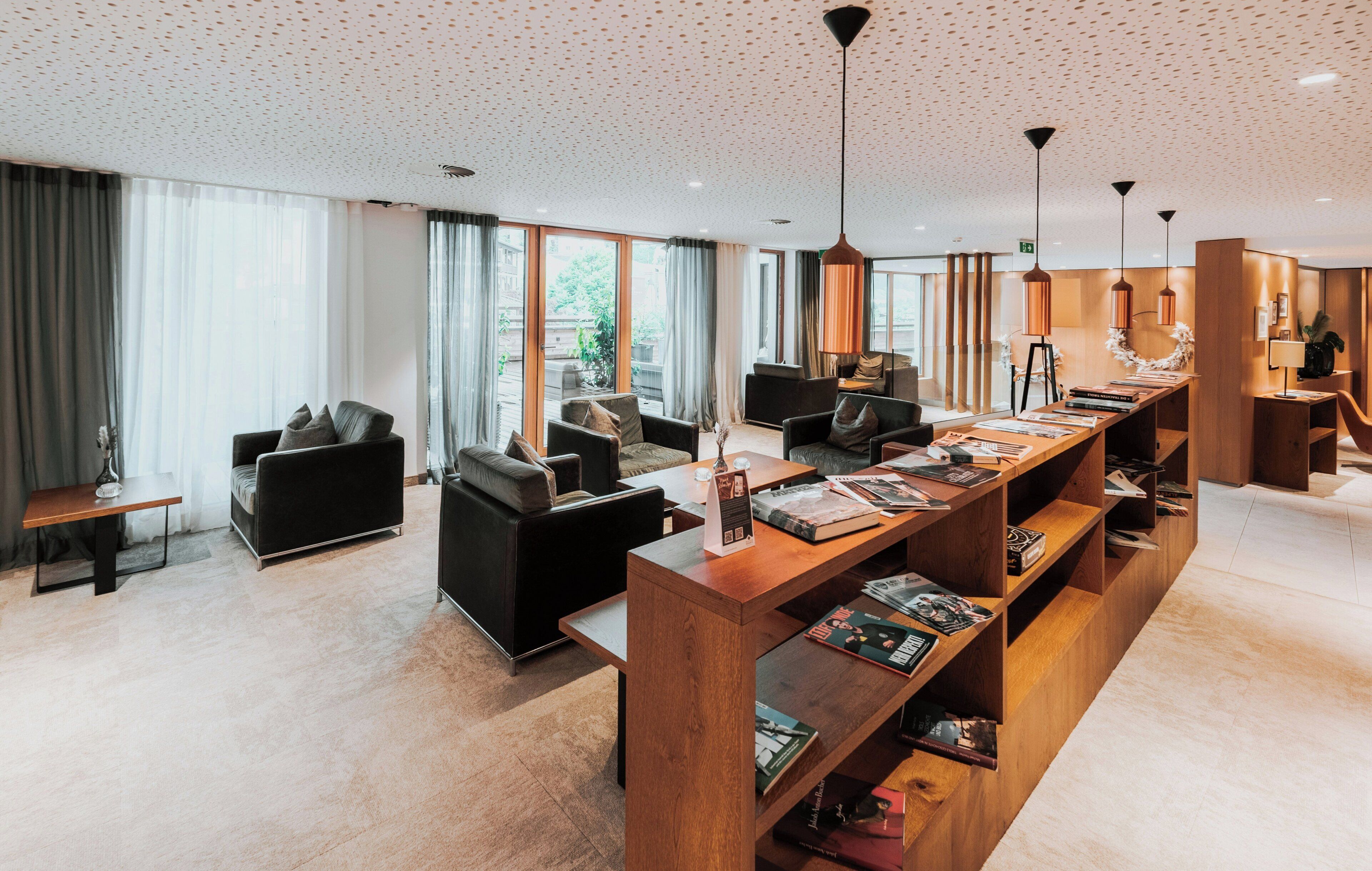 Un hall d’hôtel moderne avec un long comptoir d’accueil en bois, des canapés en cuir noir et une grande fenêtre donnant sur l’extérieur.
