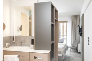 Ein modernes Hotelbad mit einem großen Spiegel, einem Waschbecken und einem Waschtisch. Ein Bett bietet Blick ins Freie.
