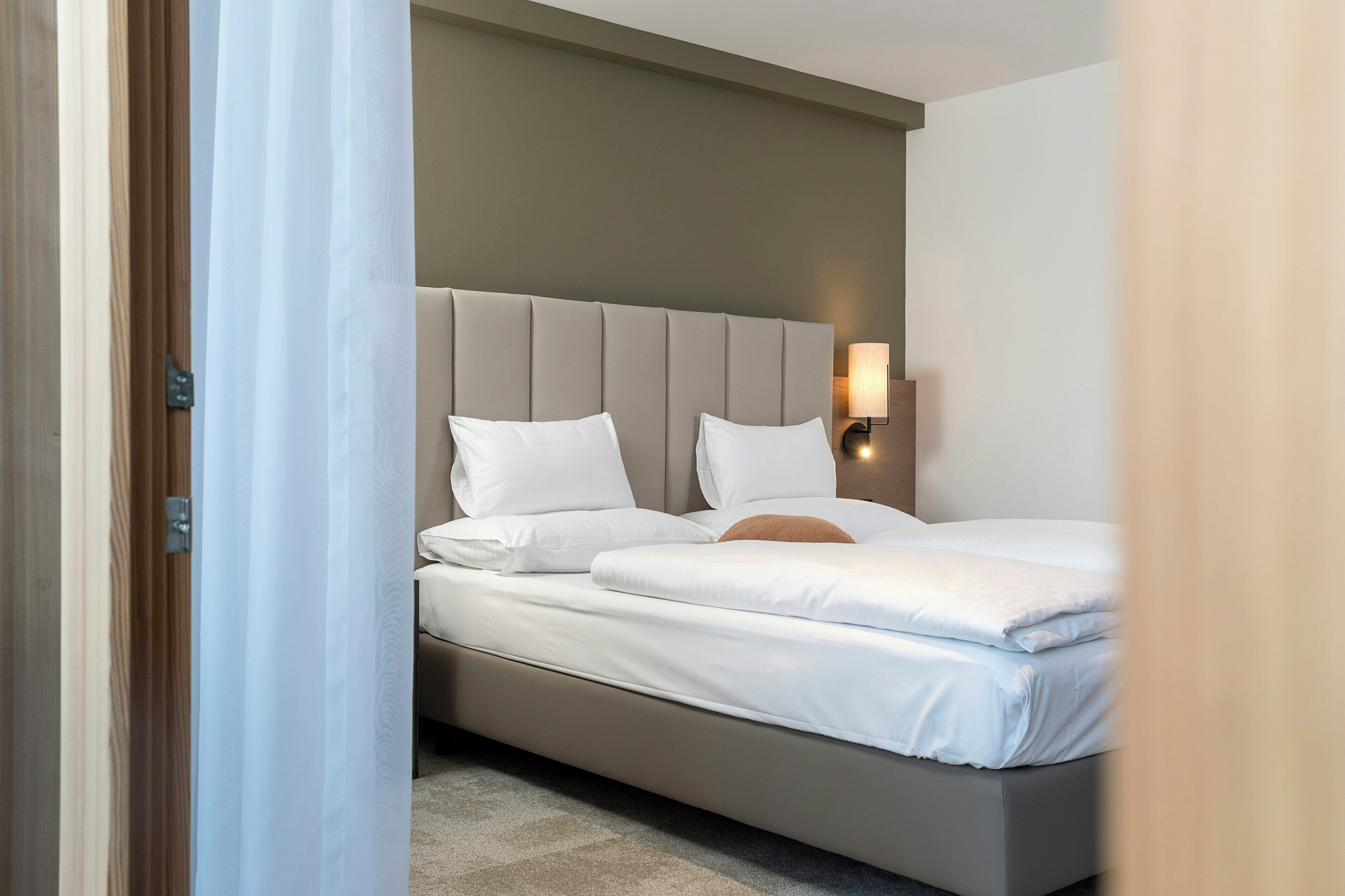 Una habitación de hotel con una cama, cabecera, lámpara de pared y una puerta.