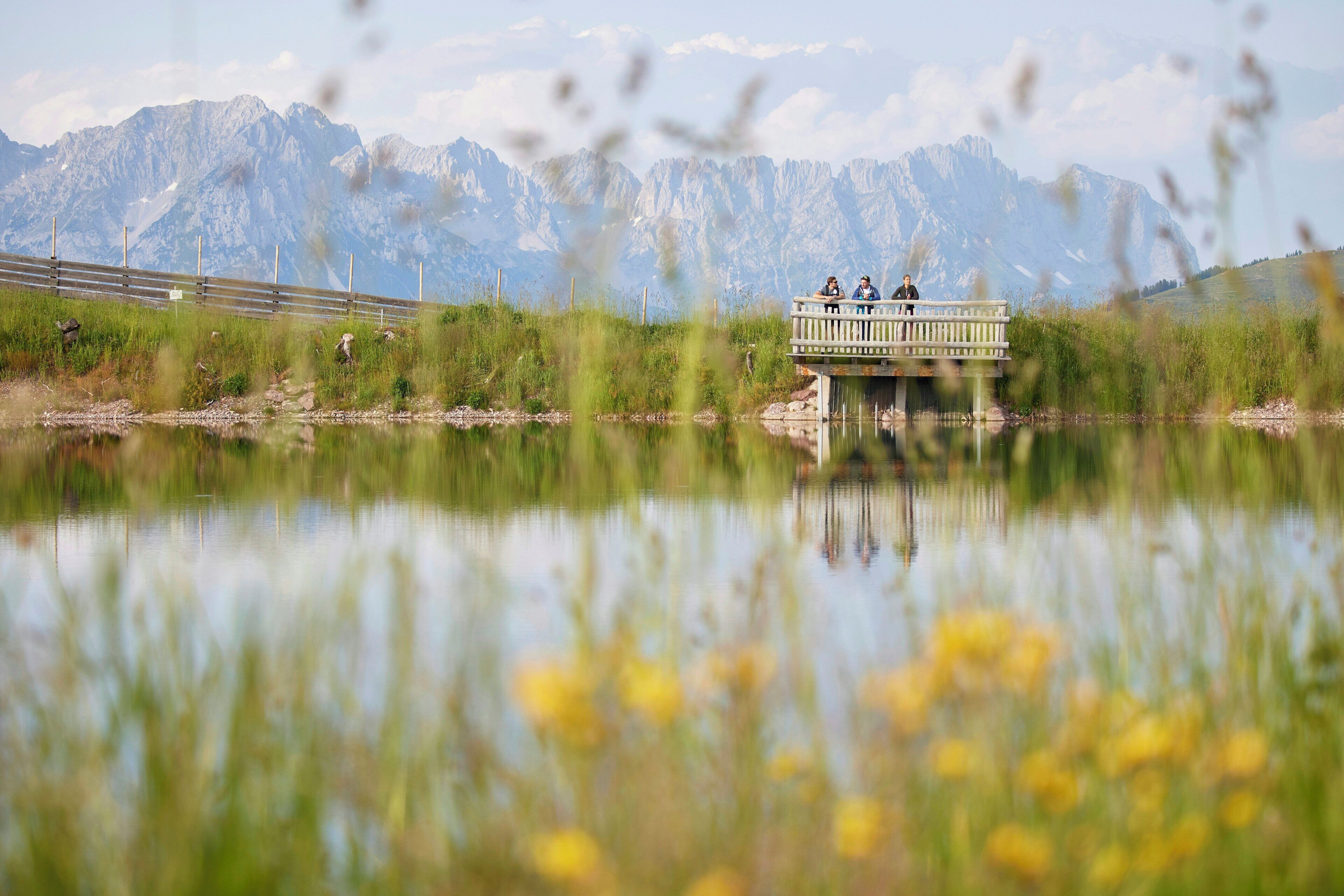 Un puente de madera sobre un lago tranquilo con montañas al fondo.