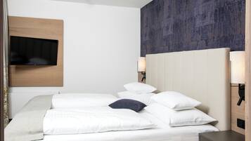 A hotel room with a bed, a flat-screen TV mounted on the wall, and a headboard with built-in lighting.