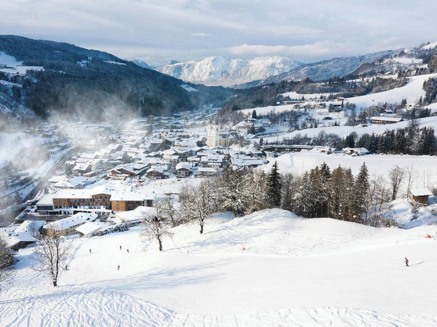 A snow-covered town with buildings, a church, and mountains in the background.