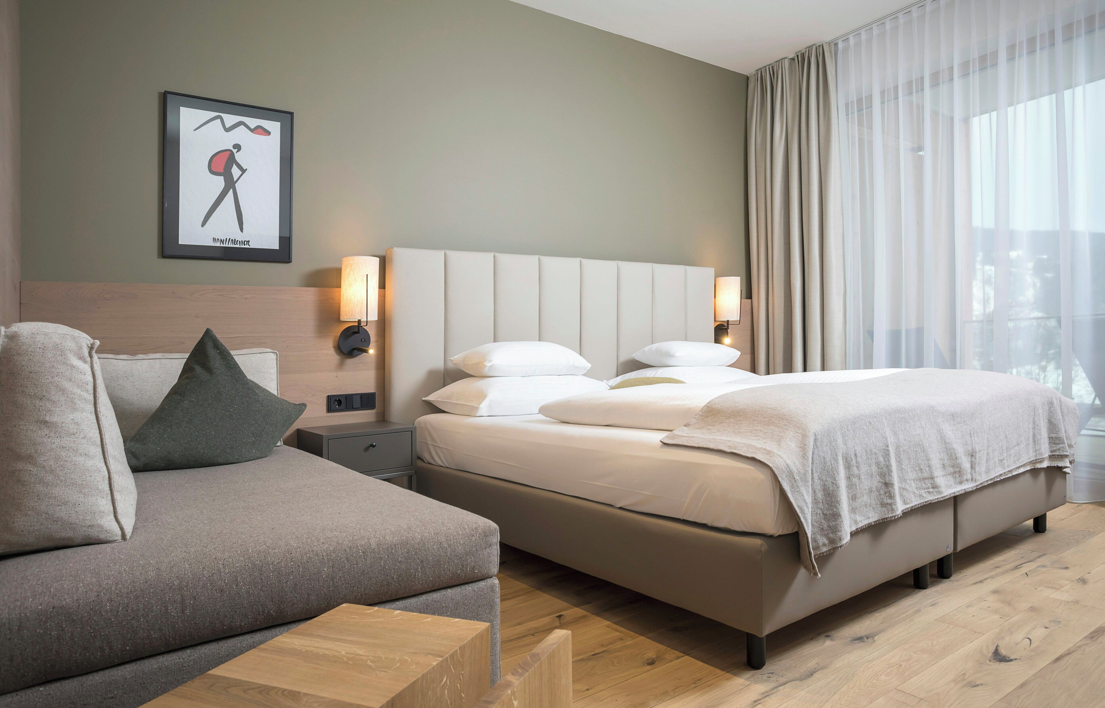 A hotel room with a bed, a sofa, a nightstand, a lamp, and a window with curtains.