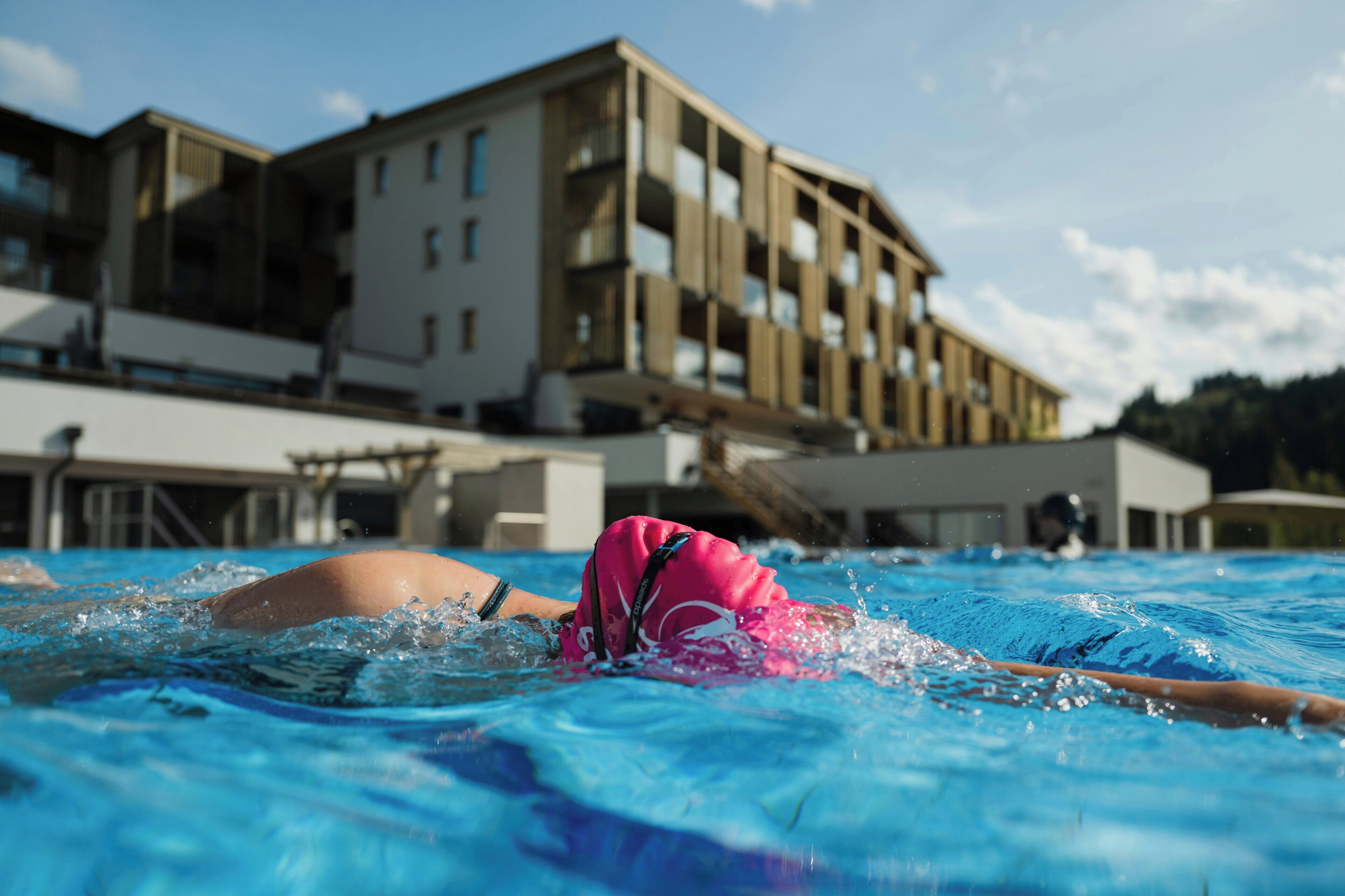Nadador en una piscina con un edificio al fondo.