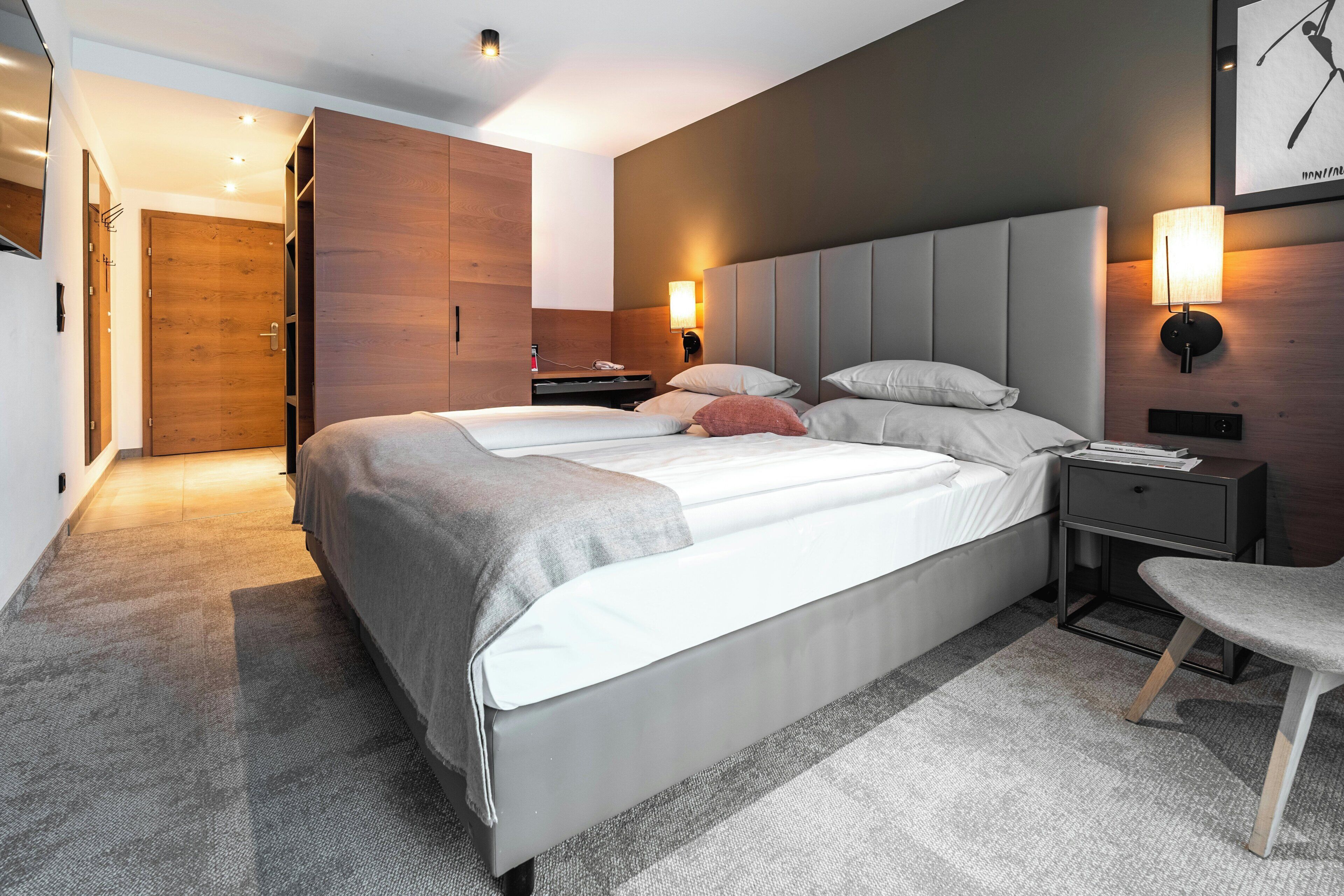 Una habitación de hotel moderna con una cama grande, mesitas de noche, una silla y un armario.