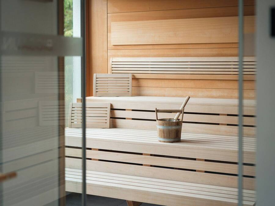 Un banco de madera con un balde pequeño y un palo, frente a una pared con listones de madera horizontales.