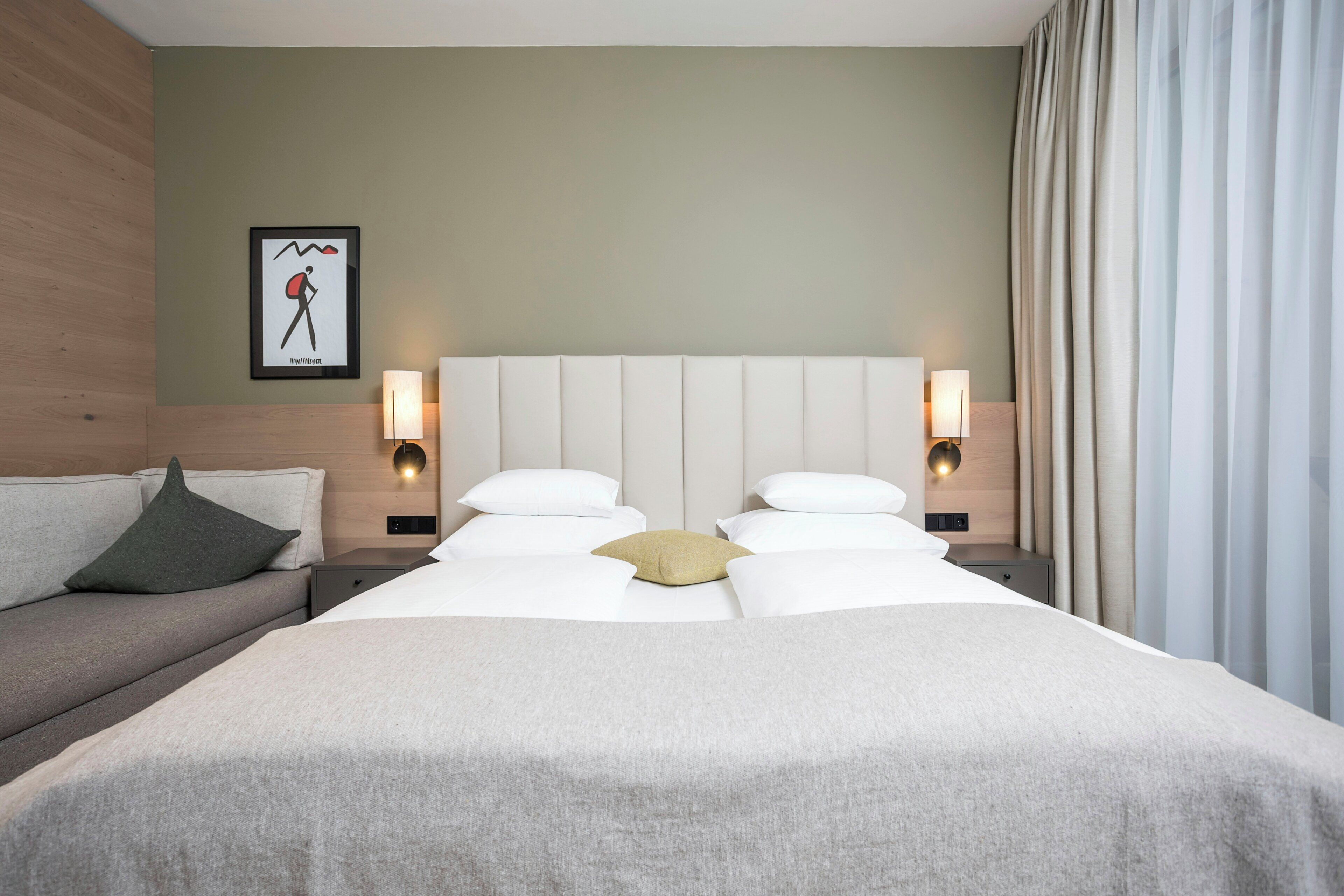 Une chambre d’hôtel avec un grand lit, deux tables de chevet avec des lampes, un canapé et un tableau accroché au mur.