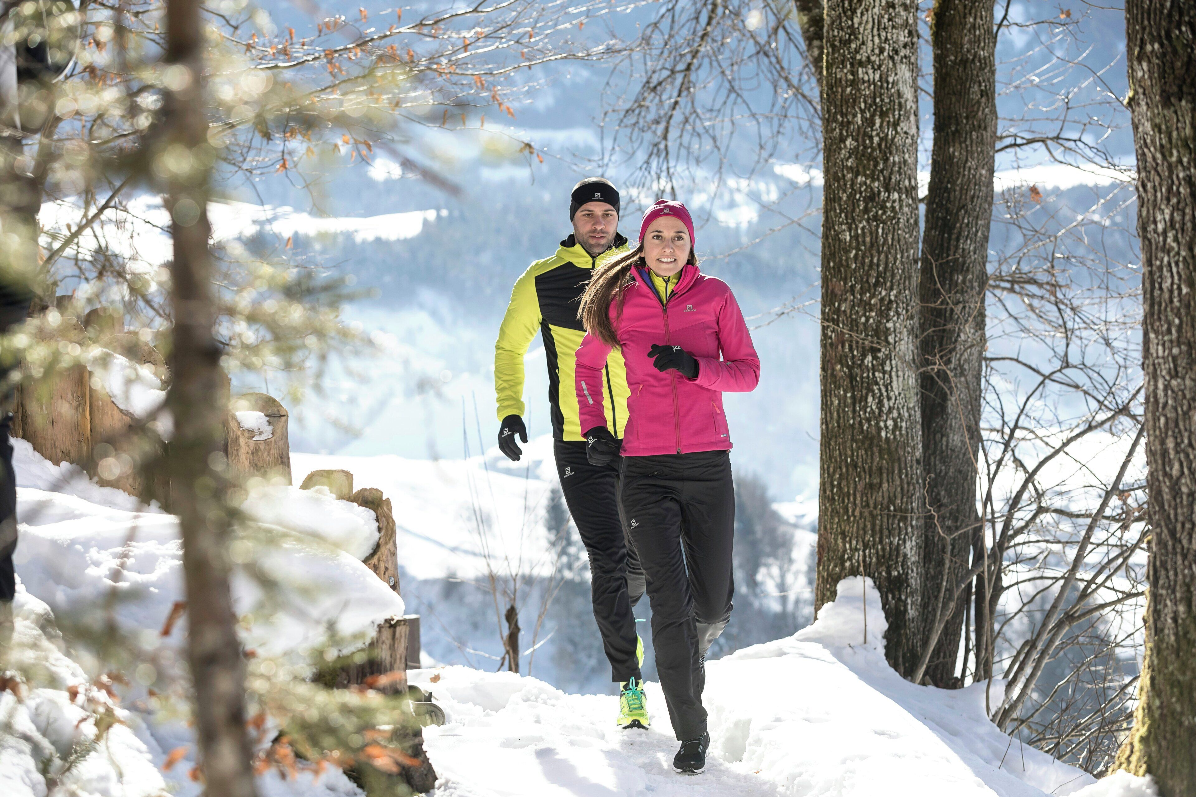 Two people walking on a snow-covered path surrounded by trees.