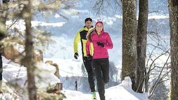 Two people walking on a snow-covered path surrounded by trees.