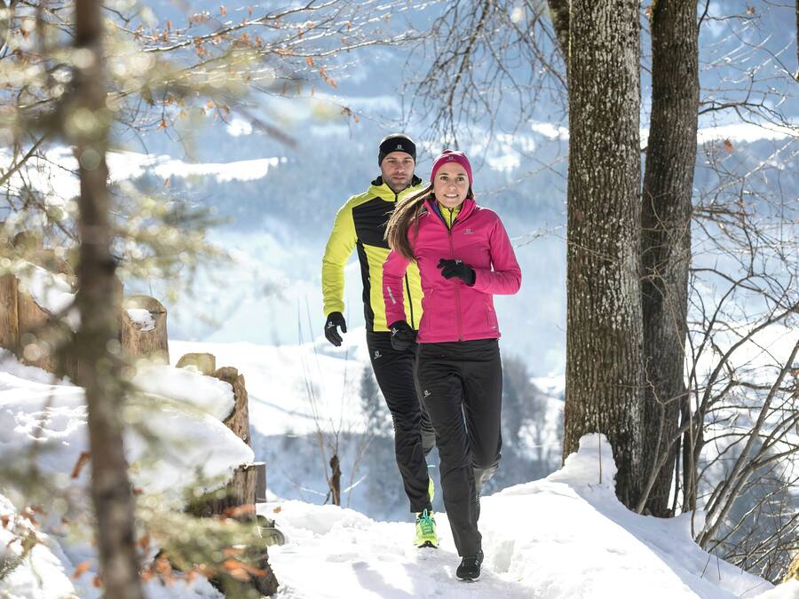 Two people walking on a snow-covered path surrounded by trees.