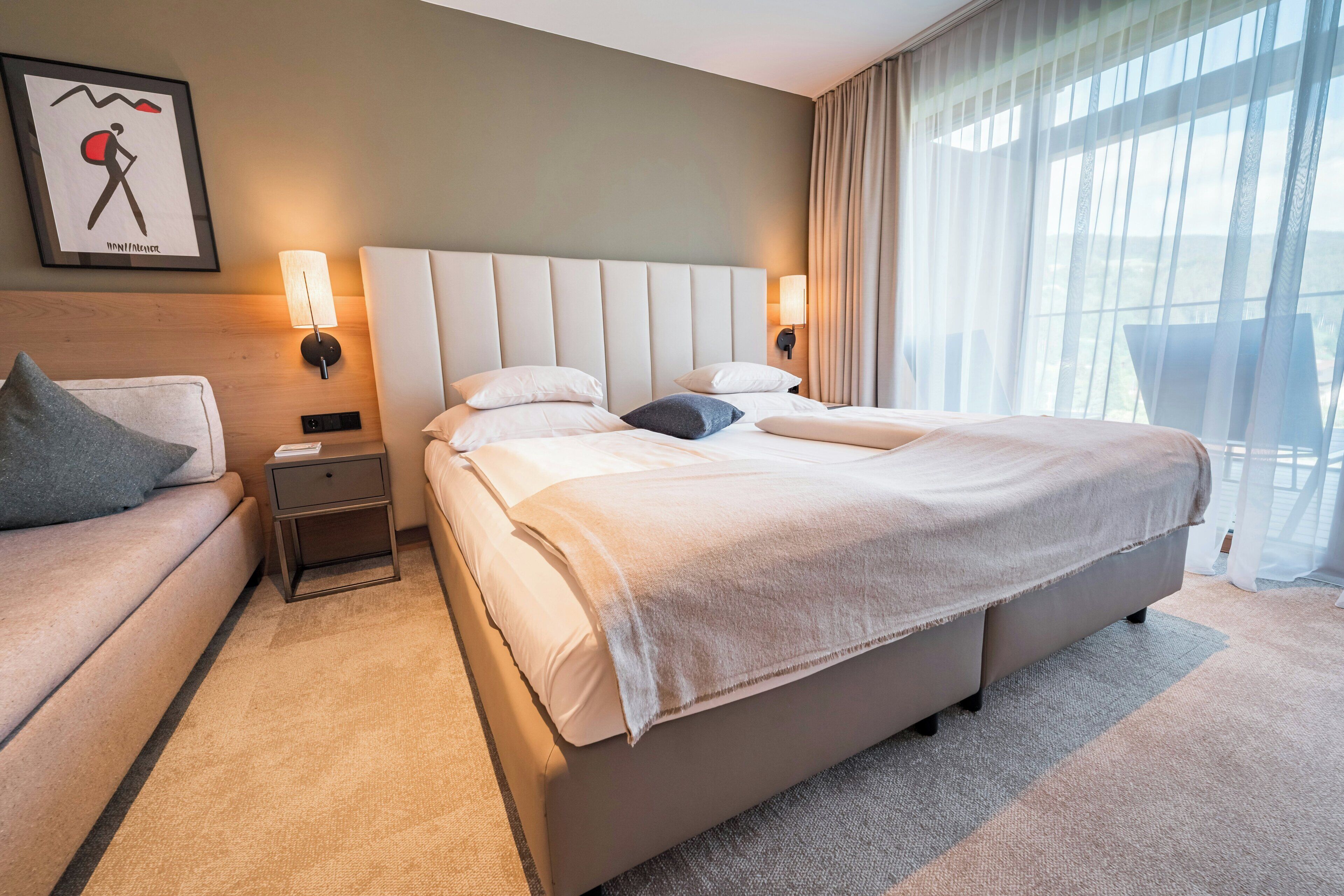 Habitación de hotel con una cama grande, una mesita de noche, un sofá y una lámpara de pared.